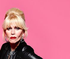 a woman with blonde hair and black leather jacket posing in front of a pink background