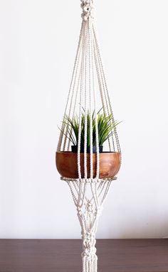 a macrame plant hanger with a potted plant in it on a wooden table