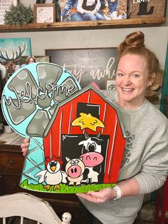 a woman holding up a cut out of a barn with farm animals on the front