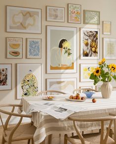 a dining room table with chairs and pictures on the wall above it, along with vases filled with sunflowers