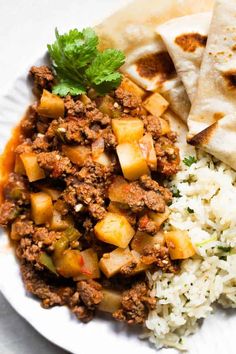 a white plate topped with rice and meat next to tortilla bread on top of a table