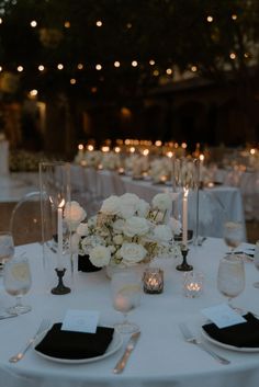 the table is set with white flowers, candles and place settings for an elegant dinner