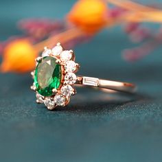 an emerald and diamond ring sitting on top of a blue surface with flowers in the background