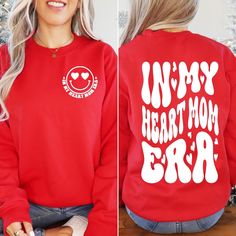 a woman wearing a red sweatshirt with the words my heart mom bra printed on it