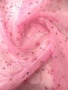 a pink scarf with flowers on it and beads in the center is laying on a white surface