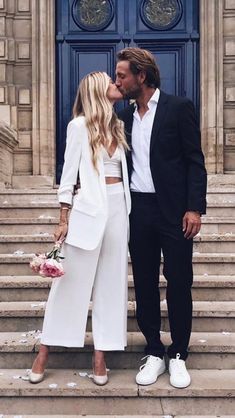 a man and woman are kissing on the steps in front of a building with flowers