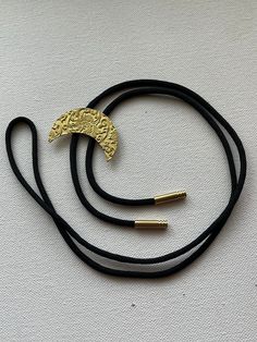 Bright yellow/gold brass crescent moon with floral pattern bolo tie necklace on black nylon cord. Gold Lariat Bolo Tie With Adjustable Length, Adjustable Gold Necklace With Sliding Knot, Gold Necklace With Adjustable Sliding Knot, Adjustable Metal Crescent Necklace, Adjustable Crescent Metal Necklace, Adjustable Gold Bolo Tie As Gift, Gold Adjustable Cord Bolo Ties For Gift, Gold Bolo Ties With Adjustable Cord As Gift, Gold Bolo Ties With Adjustable Cord For Gifts