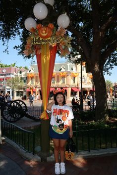 a woman is standing under a balloon arch at the disneyland california adventure park entrance with mickey mouse ears on it