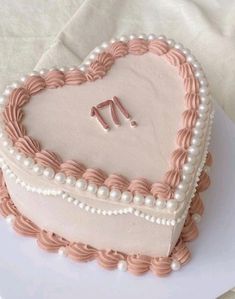 a heart shaped cake decorated with pearls and pink icing on a white tablecloth