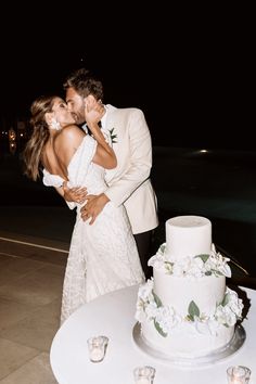 a bride and groom kissing in front of a wedding cake on a table with candles