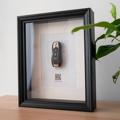 a cell phone in a black frame on a wooden table next to a potted plant