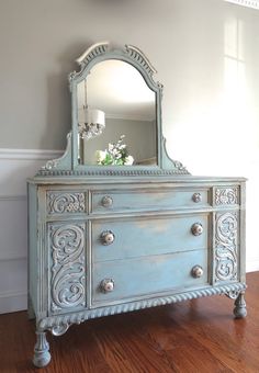 an old dresser with a mirror on top and flowers in the vase next to it