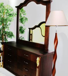 a bedroom scene with focus on the dresser and mirror, along with a large potted tree