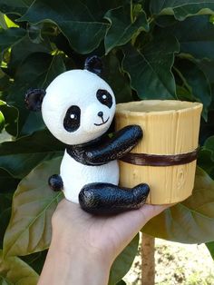 a hand holding a small toy panda bear next to a cup on a tree branch