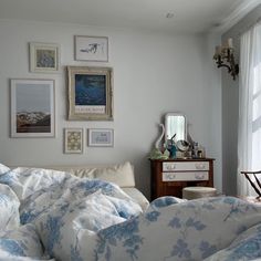 a bed with blue and white comforter in a bedroom next to a window filled with pictures on the wall