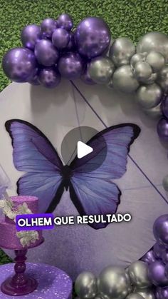 a purple cake with a butterfly on it and some balloons around the cake in the background