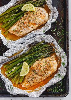 grilled salmon and asparagus in foil on a baking sheet with lemon wedges