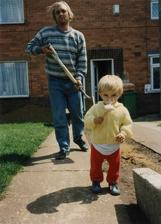 a young boy holding a baseball bat while standing next to an older man on a sidewalk