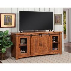 a large flat screen tv sitting on top of a wooden entertainment center next to a potted plant