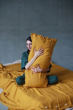 a woman sitting on top of a bed holding onto a large pillow with both hands