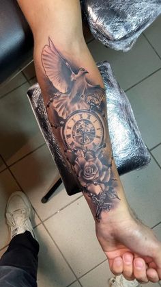 a person with a tattoo on their arm holding an alarm clock and flowers in it