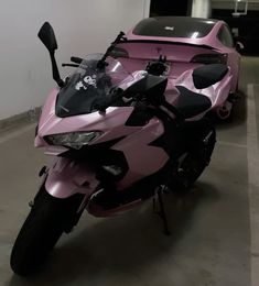 a pink motorcycle parked in a garage next to a car