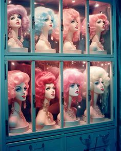 many mannequins are in a display case with pink and blue wigs