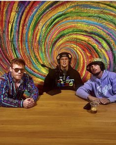 three men sitting at a table in front of a colorful wall