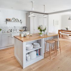 an open kitchen with white cabinets and wooden counter tops, along with two stools in front of the island