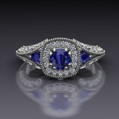 "Blue sapphires make a classic vintage style engagement ring. A round blue sapphire set in double prongs sits in a cushion-shaped diamond halo and blue sapphire trillions nestle in the split shank sides of this 14k white gold engagement ring with a bezel-set diamond on each side of the head. The top of the ring measures about 8.4mm at the widest point. The European shank at the bottom balances the whole ring out. Blue Sapphire Dimensions4.5mm EnhancementHeated ColorMedium to dark navy ClaritySli Classic Blue Sapphire Halo Ring, Classic Blue Sapphire Ring With Diamond Accents, Classic Blue Halo Ring With Accent Stones, Classic Lab-created Sapphire Ring With Halo Design, Classic Blue Halo Ring, Classic Lab-created Sapphire Ring, Classic Formal Halo Ring With Lab-created Sapphire, Classic Halo Setting Lab-created Sapphire Ring, Classic Blue Halo Ring With Round Cut