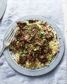 a plate filled with rice and meat on top of a white table cloth next to a fork