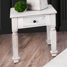 a white end table with a basket on top and a pillow sitting on top of it