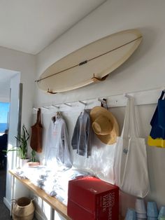 a surfboard is hanging on the wall above a table with bags and totes