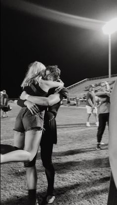 black and white photograph of two people hugging each other on a baseball field at night