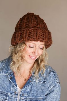 a woman wearing a brown knitted hat and denim jacket looking down at her cell phone