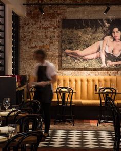 a man standing in front of a painting on the wall next to tables and chairs