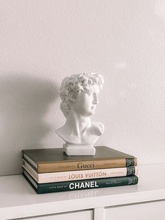 a stack of books sitting on top of a white dresser next to a busturine