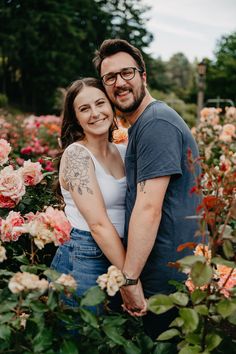 a man and woman standing in front of flowers with their arms around eachother