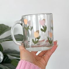 a person holding a glass mug with flowers on it