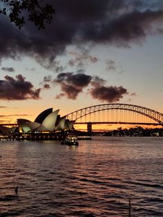 the sydney opera house and harbour bridge at sunset with clouds in the sky above it