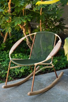 a green rocking chair sitting on top of a cement floor next to trees and bushes