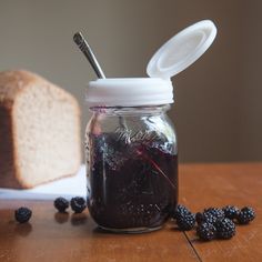 a glass jar filled with blackberries next to a loaf of bread