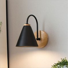 a wall light with a black shade hanging from it's side next to a potted plant