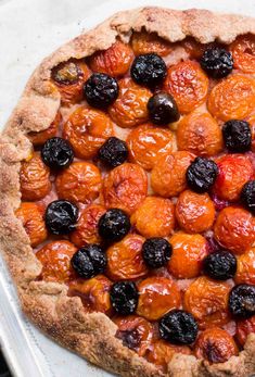 a close up of a pie on a pan with cherries and black olives