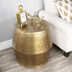 a gold colored table with a clock on it next to a white chair and pillow