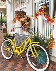 a yellow bicycle is parked in front of a white house with autumn decorations on the porch