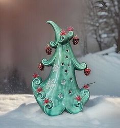 a green ceramic christmas tree with red berries on it's top in the snow