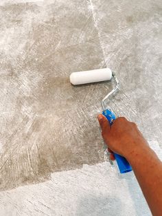 a person using a roller to paint concrete on the floor with a blue rag and white brush