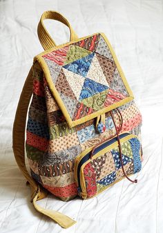 a multicolored patchwork backpack sitting on top of a white sheet covered bed