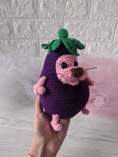 a hand holding a crocheted stuffed animal in the shape of a purple eggplant